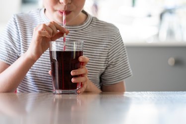 person in a black and white striped shirt drinking diet soda from a glass with a red and white striped straw