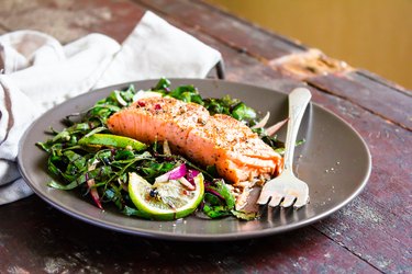 A black plate of salmon fillet roasted with spices served with spinach and lime as examples of foods for sexual health for women