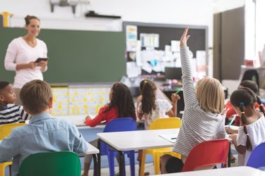 Caucasian schoolgirl raising hand with his classmates surround of her