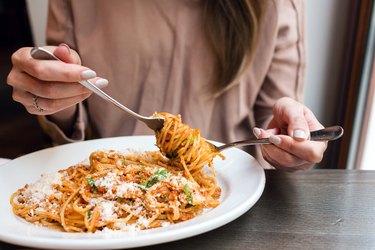 girl eating starchy spaghetti Bolognese, winding it around a fork with a spoon.