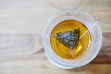 Top view of clear glass cup with green tea bag steeping on wooden table