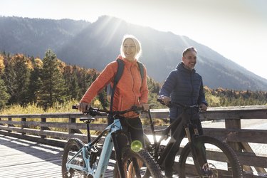 Couple with mountain bikes crossing a bridge, getting their daily recommended amount of cardio