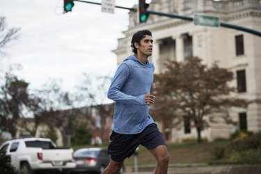 Young Latino man in blue sweatshirt runs by small town courthouse