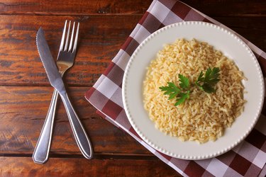 organic brown rice grain cooked in white dish on rustic wooden table. Integral rice Top view