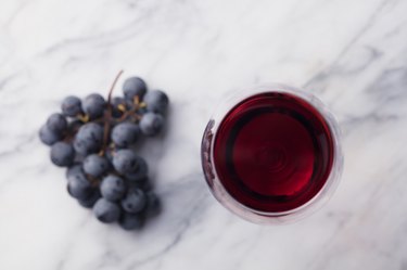 Red wine in glass with fresh grape on marble table background. Top view.