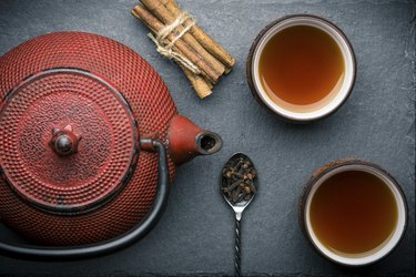 Tea composition with ceramic tea cups and red iron teapot on dark stone background