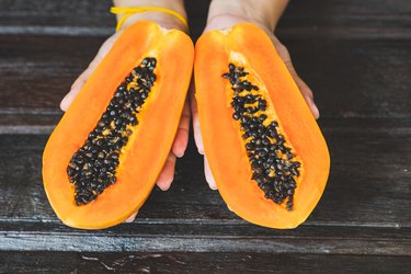Cropped Hand Of Woman Holding Halved Papayas