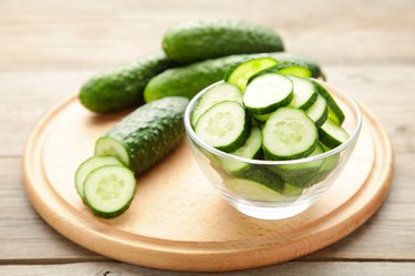 Fresh cucumber slices in bowl on grey wooden background.