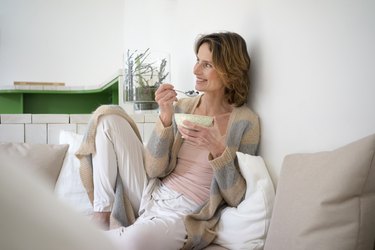 Relaxed smiling mature woman sitting on bench eating healthy food, as a way to promote healthy aging