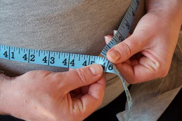 Close view of a person using a measuring tape to measure their belly fat