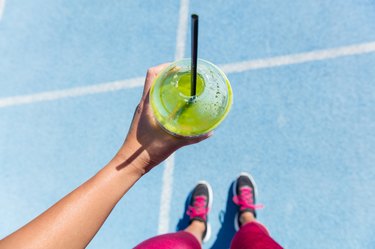 Runner drinking a green smoothie on running track before a marathon