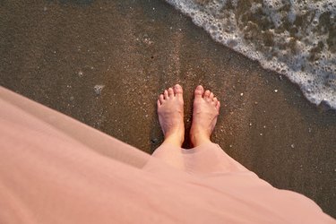 top-down photo of a person's feet standing on a beach near bubbling waves