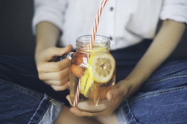 Cropped shot of person drinking homemade fresh summer drink from mason jar with straw