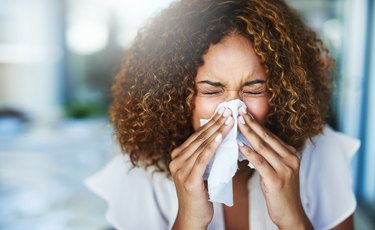 woman with allergies blowing her nose too hard, which can cause a nosebleed