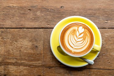 Top view of hot cappuccino coffee in a yellow cup with latte art on wooden table background.