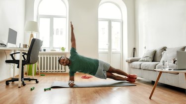 Person wearing green T-shirt and shorts performing side plank exercise in living room.