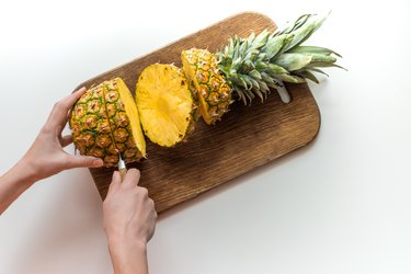 person cutting fresh pineapple on wooden board