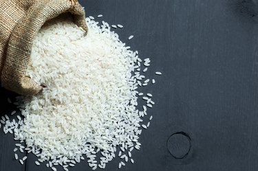 turkish raw white rice grains in burlap sack on black wooden background