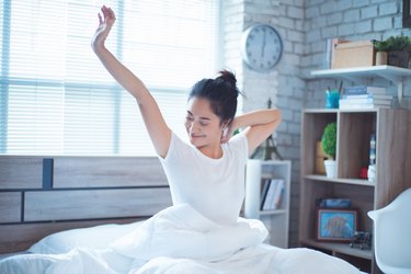 An Asian woman waking up in bed and feeling refreshed and energetic