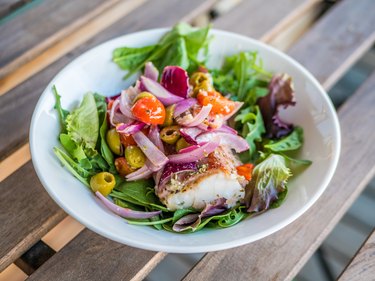 Cod fillets salad wrapped in bacon in white plate on wood table.