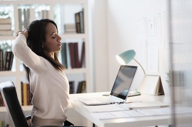 Mixed race businesswoman stretching at desk