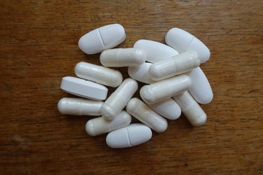 Heap of white caplets of calcium citrate and capsules of magnesium citrate on wood