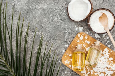 top view of coconut oil in bottles on wooden board on grey textured background with copy space and palm leaf