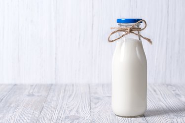 Bottle and glass of milk with straws, wooden background