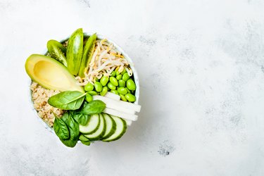 Vegan, detox green Buddha bowl recipe with quinoa, avocado, cucumber, spinach, tomatoes, mung bean sprouts, edamame beans, daikon radish. Top view, flat lay, copy space