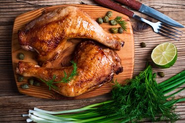 Two chicken legs, green onion, dill and lime on wooden board viewed from above