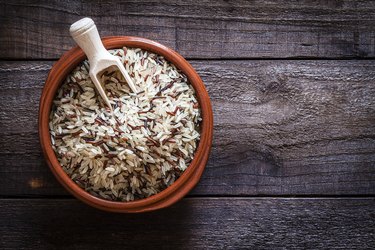 Brown bowl filled with red and brown rice grains shot from above on wooden table