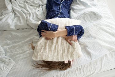 A woman in bed, covering her face with a pillow, suffering from insomnia due to gut problems