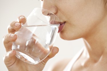 Young woman drinking glass of water wondering if you can drink gatorade while fasting and if gatorade zero breaks a fast