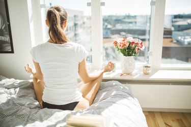 Back view of a woman sitting in bed doing a morning meditation