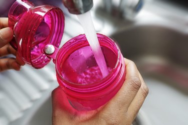 Detail of hands filling pink water bottle at a sink