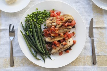 White plate with chicken breast and green beans.