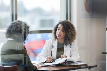A doctor wearing a white coat and stethoscope and patient sitting in doctor's office in front of a window, discussing treatment options for bloody stools