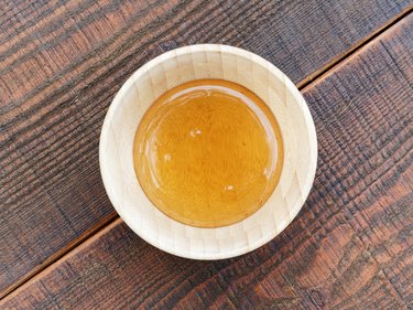 Fresh honey in wooden honey bowl on wooden table, top view.