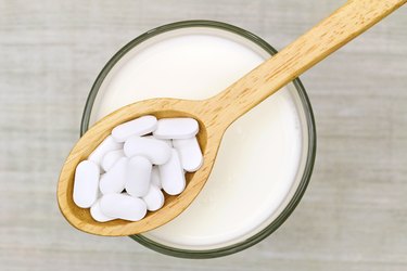 Wooden spoon of Calcium carbonate tablets above glass of milk