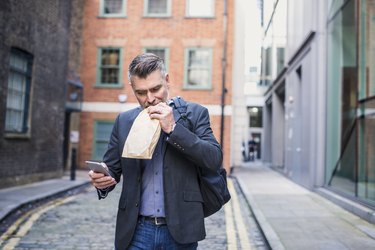 Businessman eating a sandwich and using smart phone