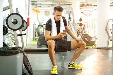 Young handsome man using phone while having exercise break in gym.