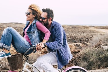 happy adult caucasian, couple having fun with bicycle in outdoor leisure activity. concept of active playful people with bike during vacation - everyday joy lifestyle without age limitation - man carry woman and both have fun and laugh a lot with wind in