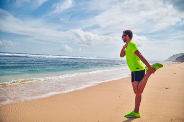 Man doing runner's knee exercises and stretches on a beach.