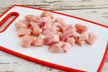 Chicken fillet cut in cubes on a white cutting board. Step by step cooking