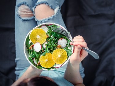 Woman in jeans at bed, holding vegan salad bowl