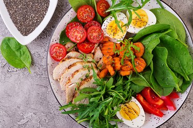 Plate with a keto diet food. Cherry tomatoes, chicken breast, eggs, carrot, salad with arugula  and spinach. Keto lunch. Top view