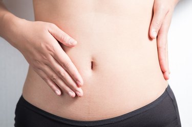 Female hands protecting the bloating stomach on white background.