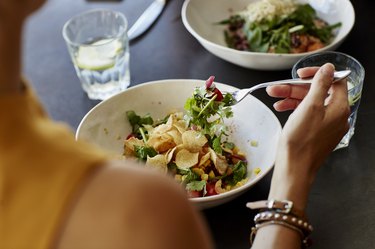 View from the back of a person eating a salad with leafy greens, corn, tomato and potato chips for weight loss