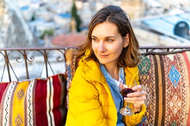 Woman is enjoying the glass of wine on the balcony at sunset