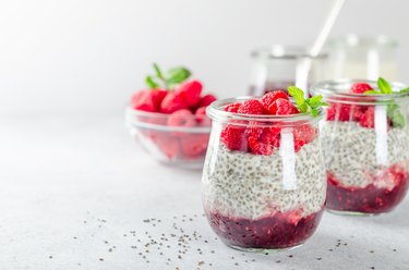 Two glass jars with chia pudding with raspberry and jam. Bowl of